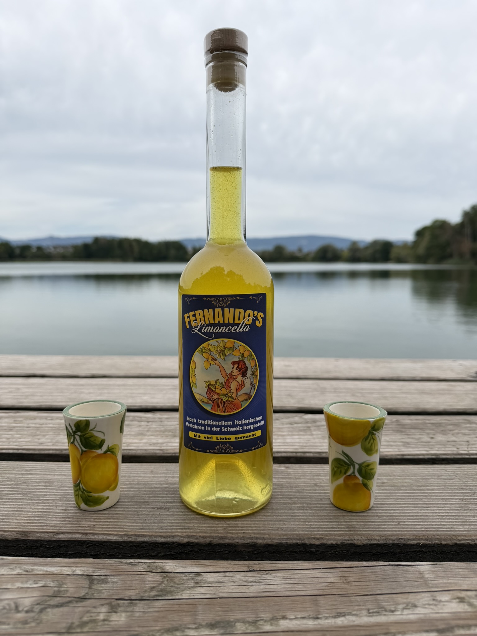 Fernando’s Limoncello mit zwei Zitronenbechern auf einem Holztisch am See